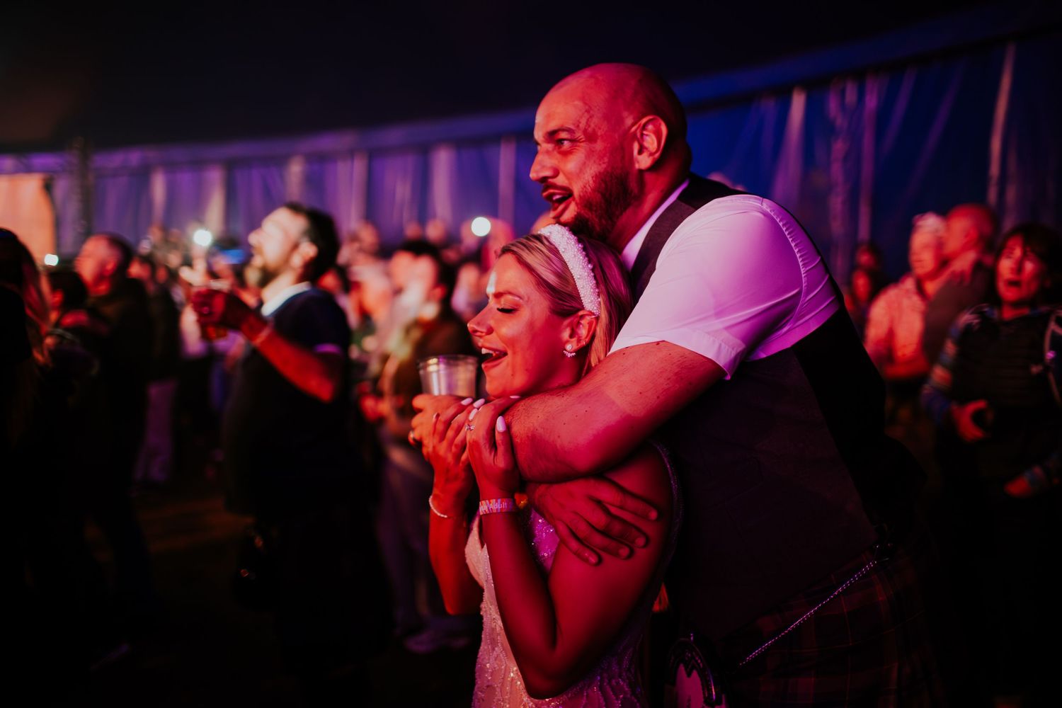Romantic dance moment between couple at dimly lit wedding celebration with pink lighting.