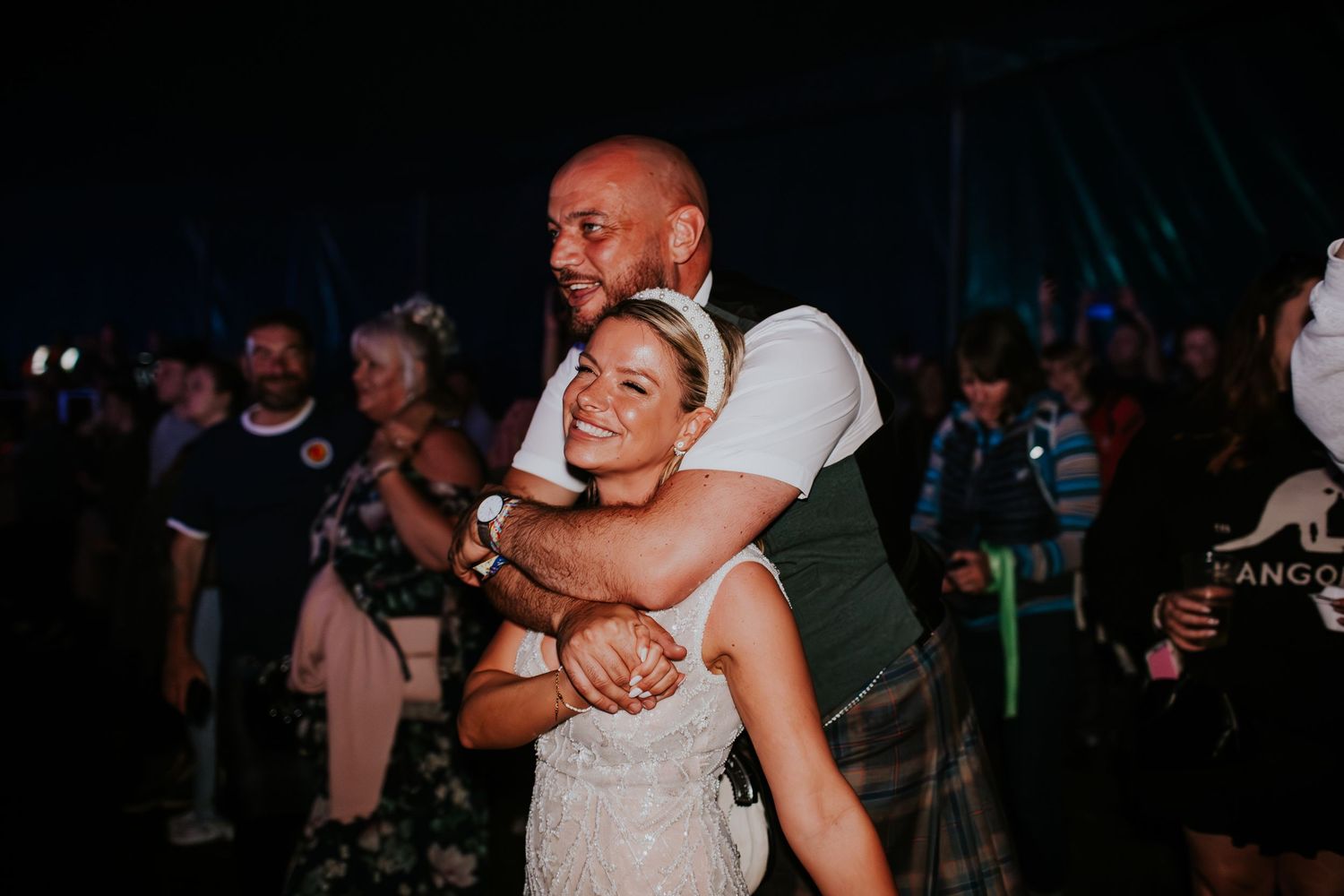 Two people dancing and embracing at a lively nighttime event with a dark crowd in the background.