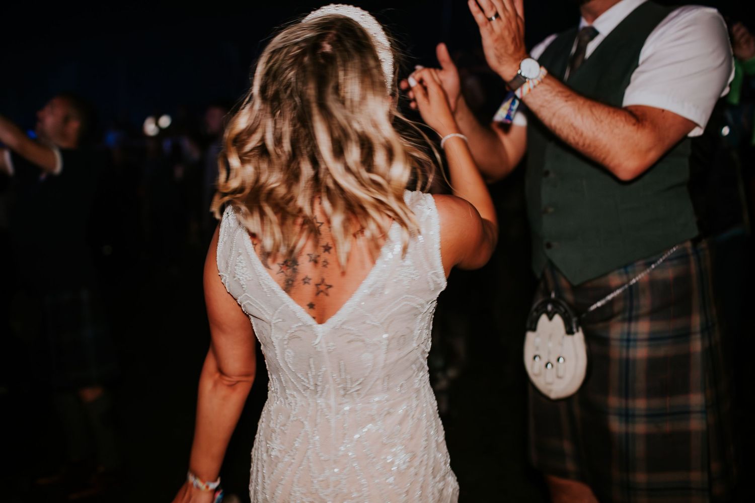 A couple in traditional Scottish attire dances together at a nighttime celebration.