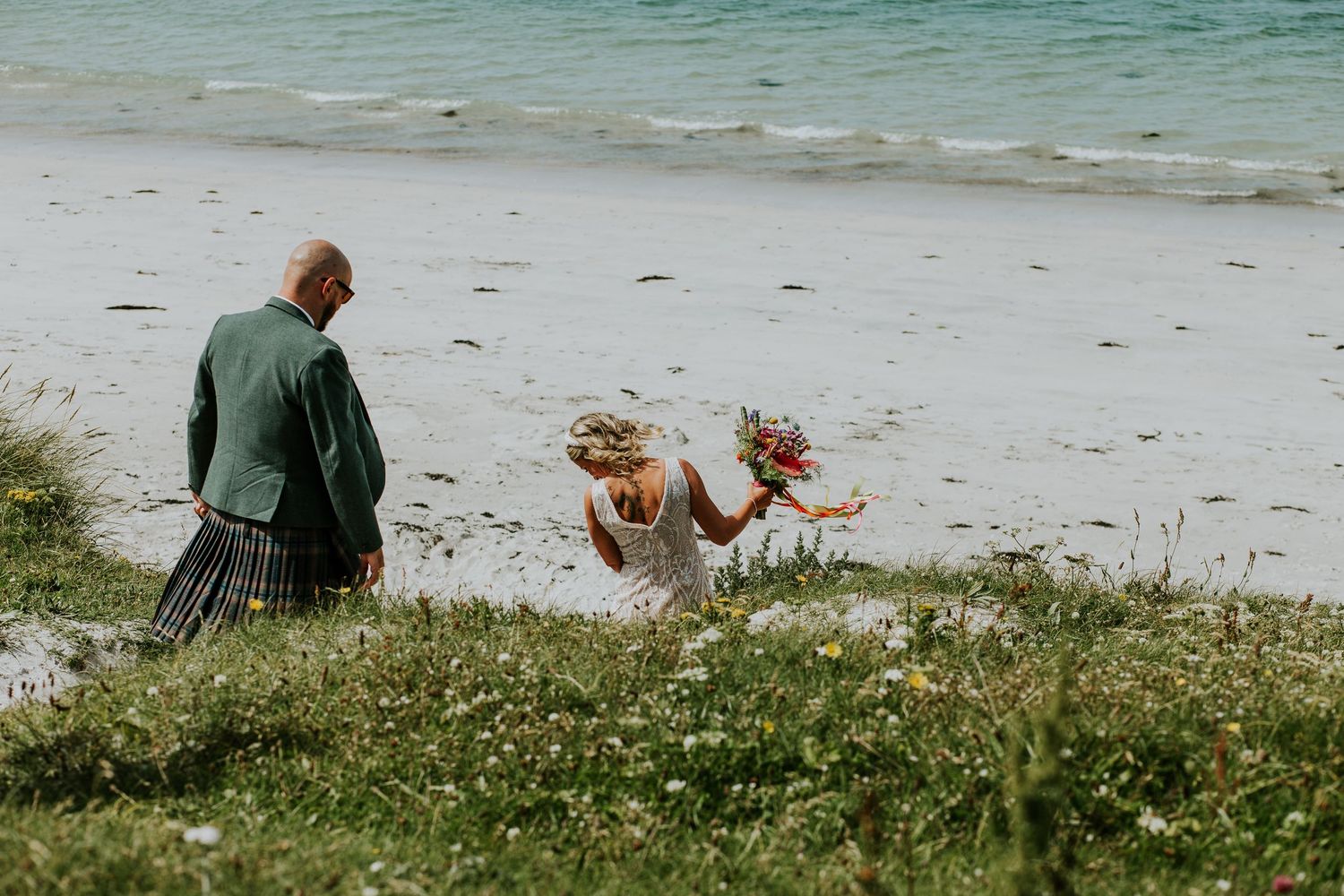 Group of friends enjoying a sunny day at a beach with grass and wildflowers in the foreground.