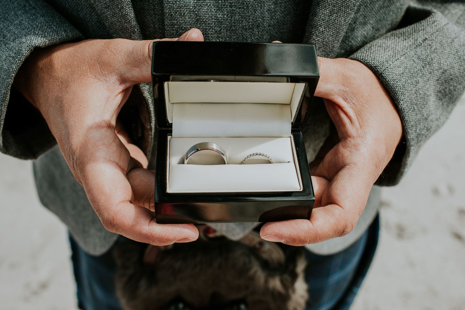 Hands holding a small black box with two wedding rings nestled inside.
