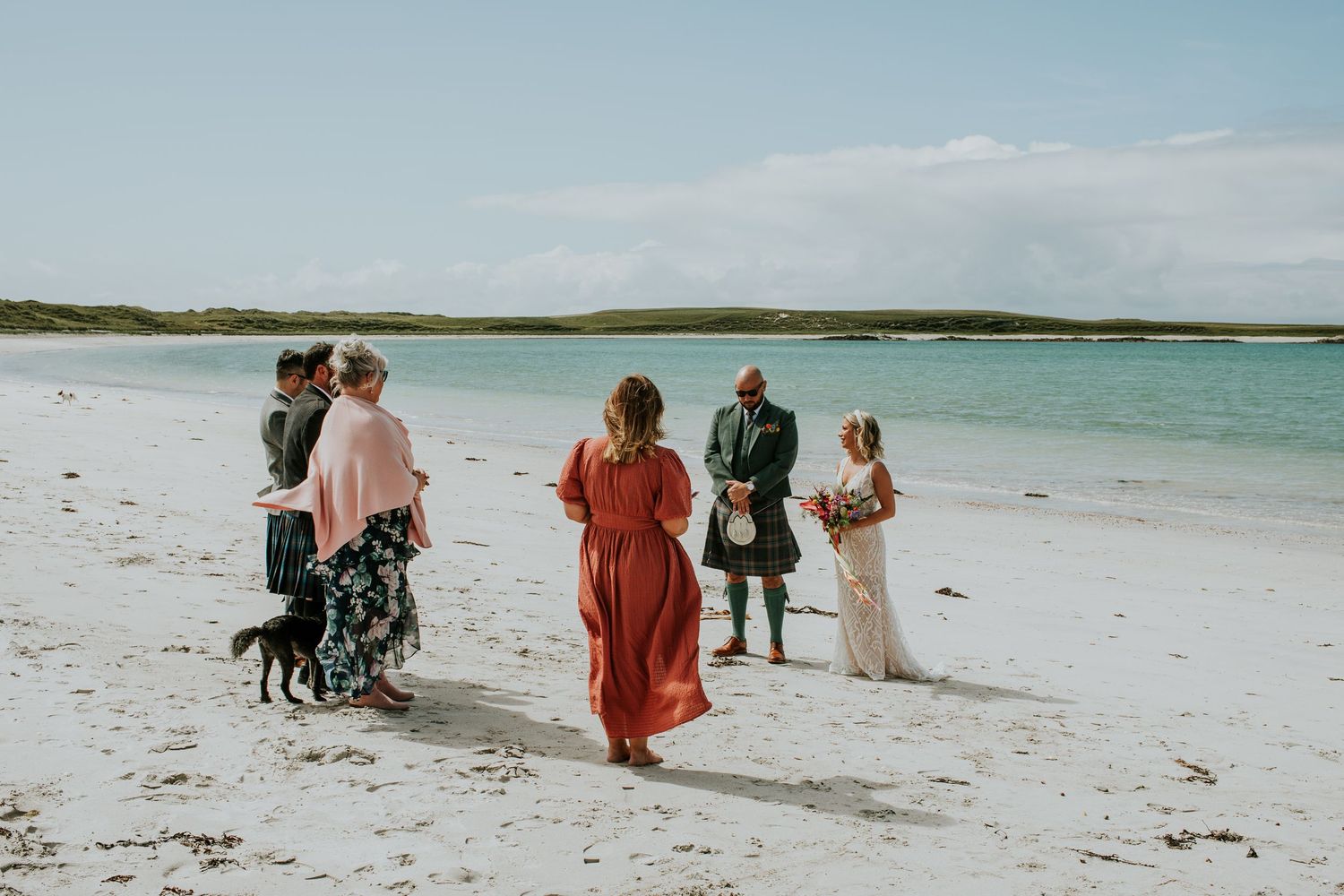 Small group of people and a dog walking together on a pristine white sandy beach with turquoise water.