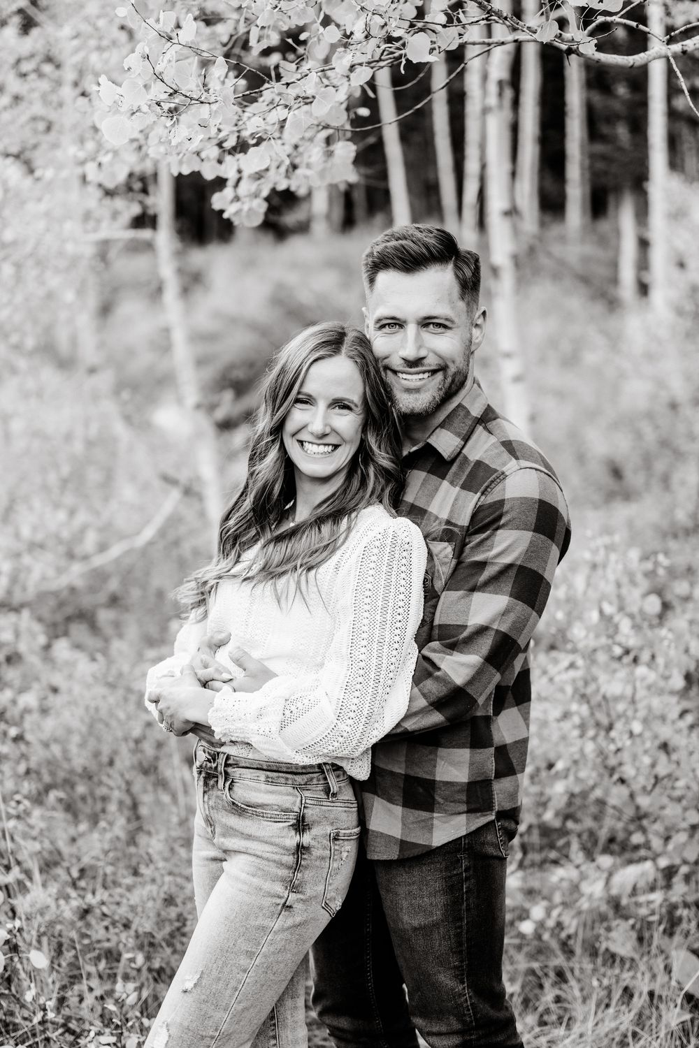A loving couple in coordinated casual wear embraces while posing for a black and white portrait in nature.