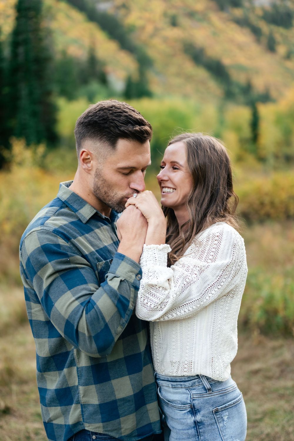 A romantic couple share an intimate moment in a mountain meadow surrounded by autumn foliage.