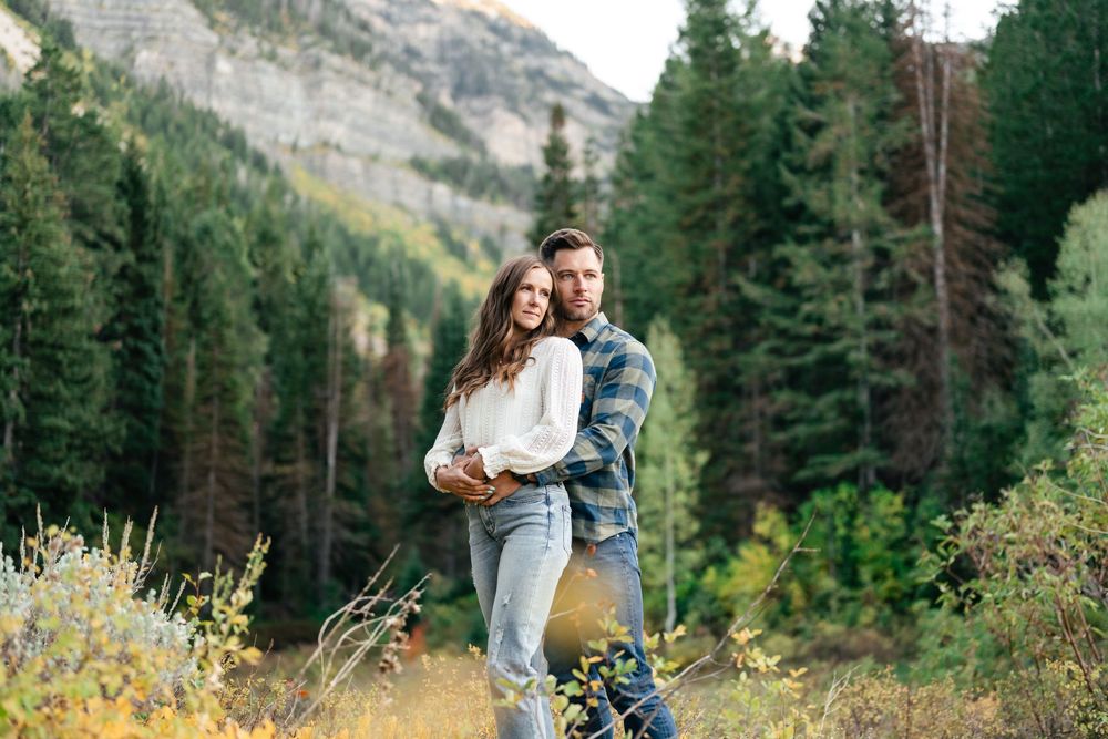 A couple shares an intimate moment against a backdrop of evergreen trees and mountain peaks.