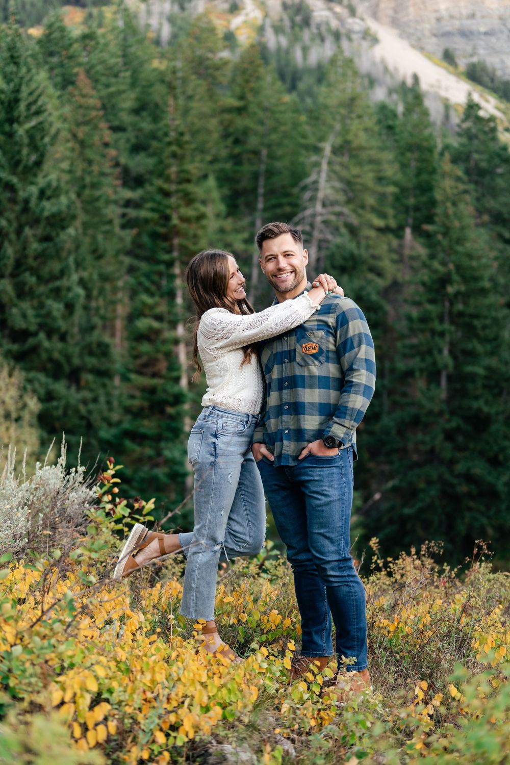 A couple sharing a tender moment among yellow wildflowers with mountain scenery behind them.