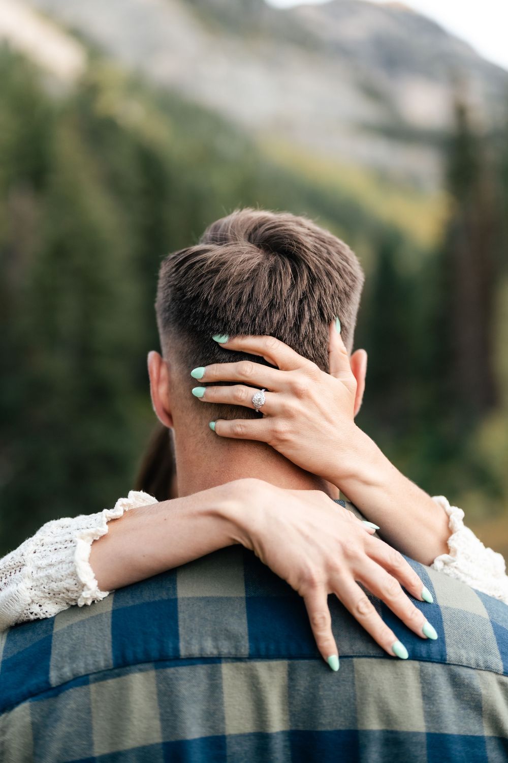 Close up of hands with turquoise ring embracing from behind against mountain landscape.