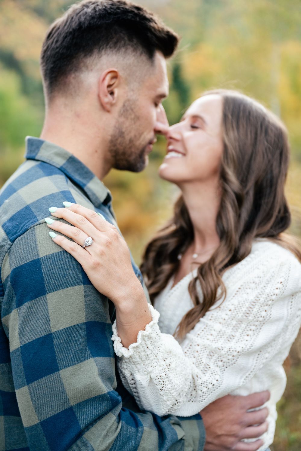 A romantic engagement photo showing a close embrace, with a sparkling ring visible on the woman's hand.