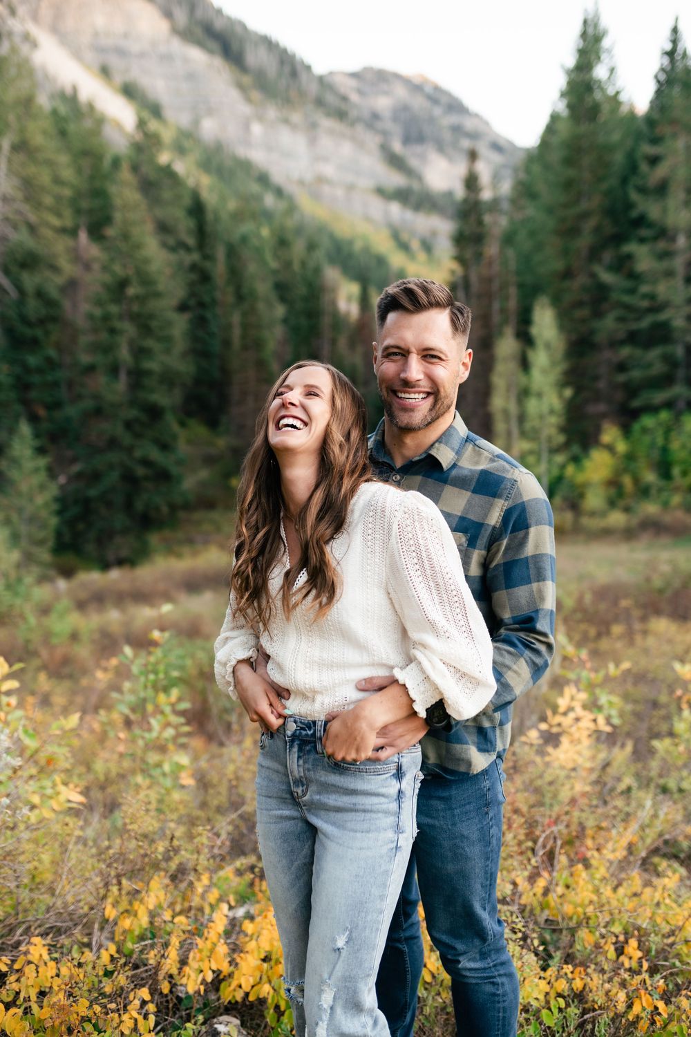 Joyful couple in casual attire sharing intimate moment against scenic mountain wilderness background.