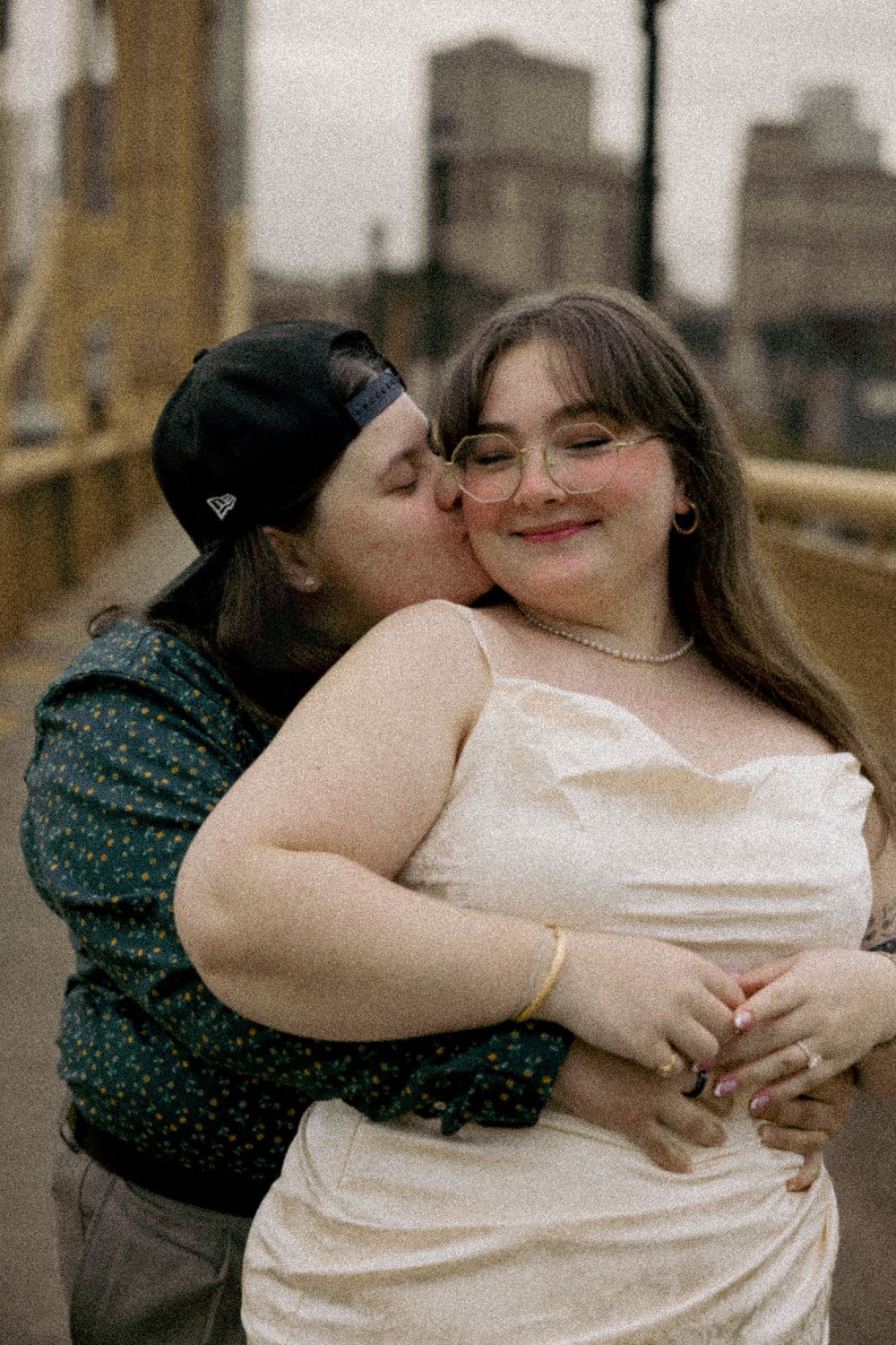 A tender moment captured between two people embracing on a rooftop with city buildings in the background.