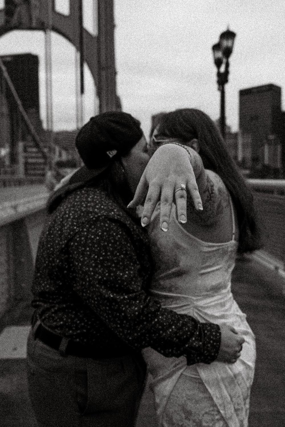 A romantic moment shared between a couple embracing on a city bridge at dusk with a street lamp in view.