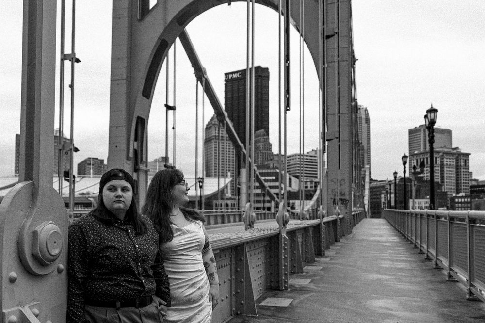 Two people stand together on the Andy Warhol Bridge in Pittsburgh while viewing the downtown skyline in black and white.
