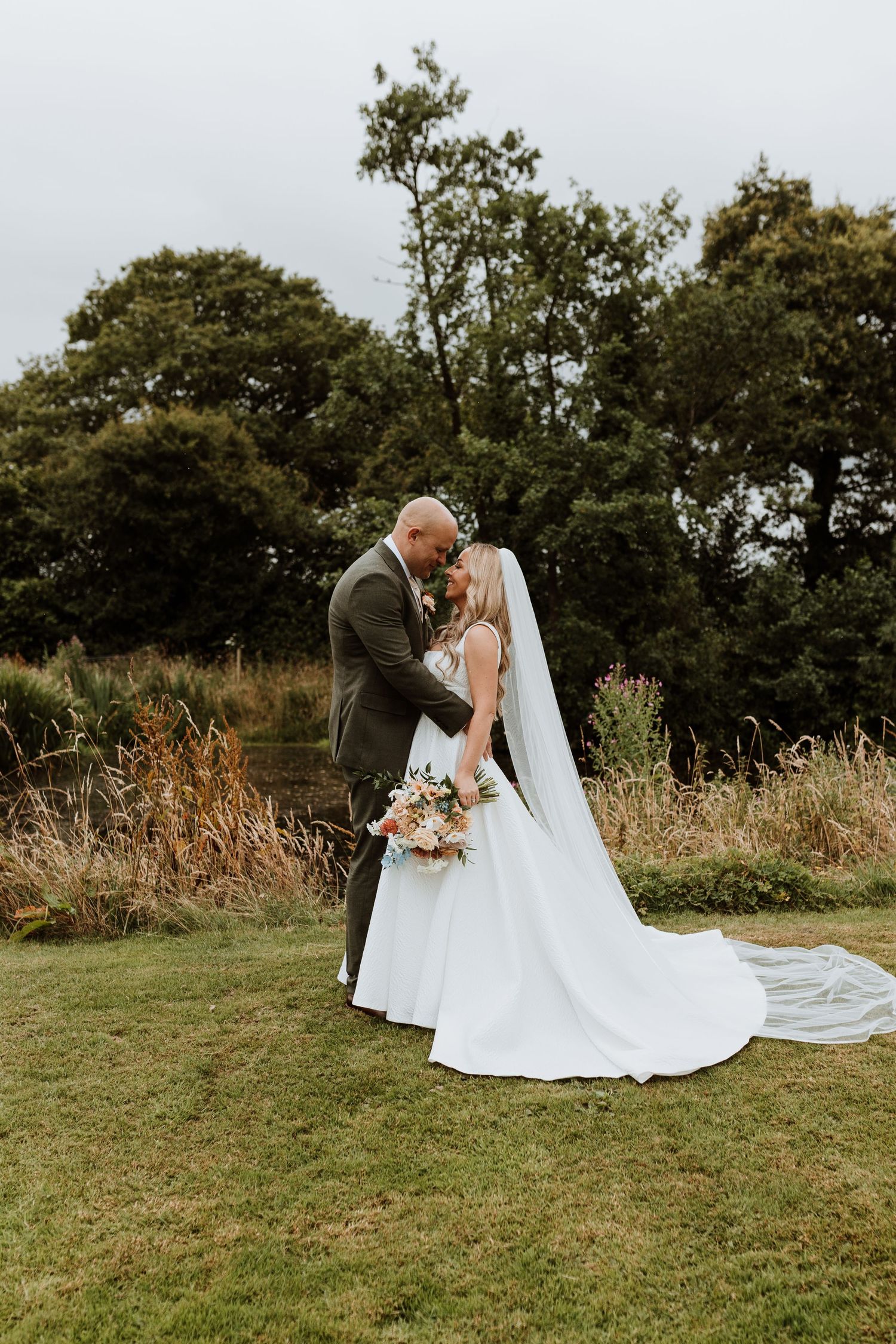 Wedding couple sharing an intimate moment near the lake with autumn trees in the background at Stanford Farm