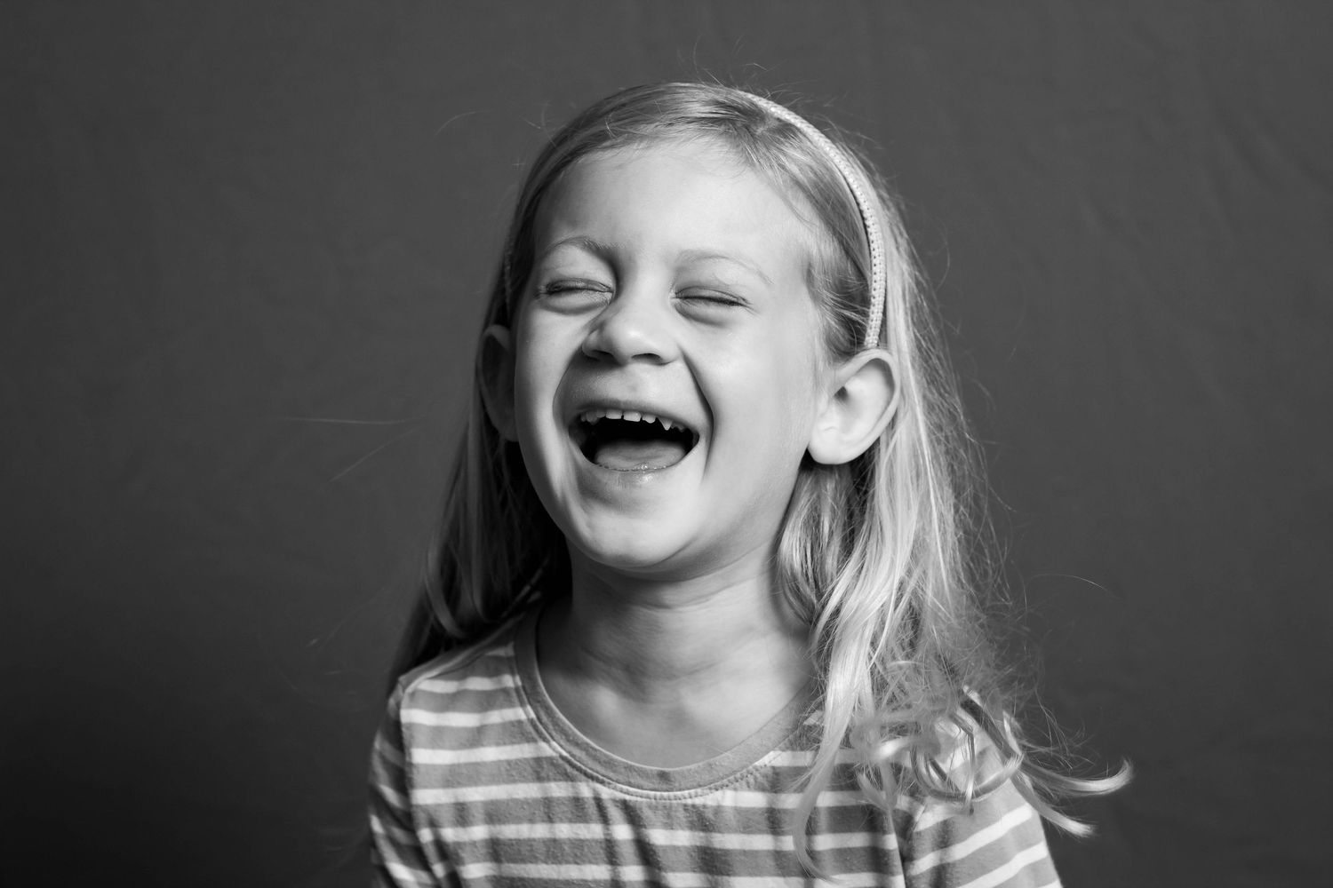 A black and white portrait of a young child laughing joyfully while wearing a striped shirt.