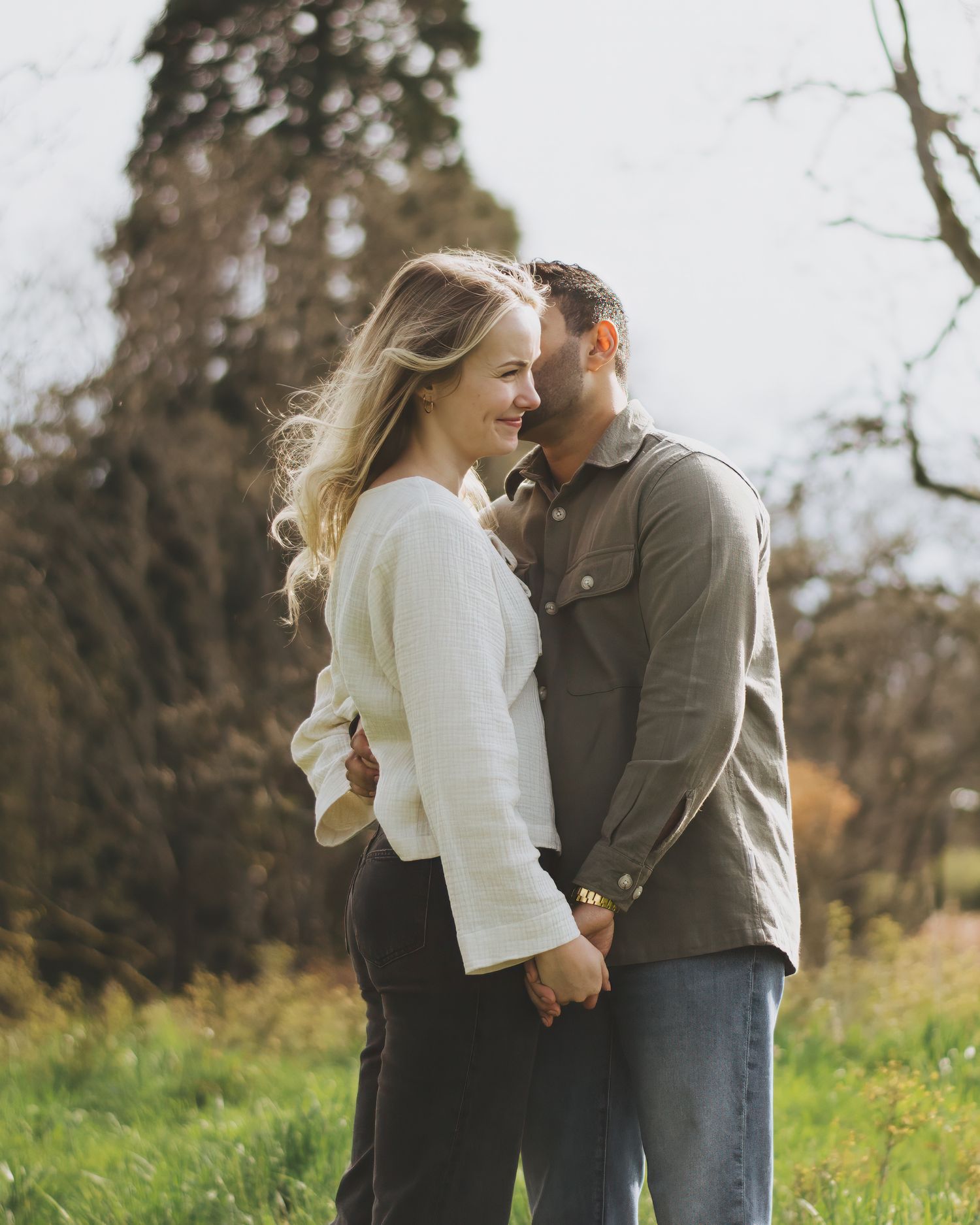 A couple sharing an intimate moment together in a natural outdoor setting with tall grass and trees in soft lighting.