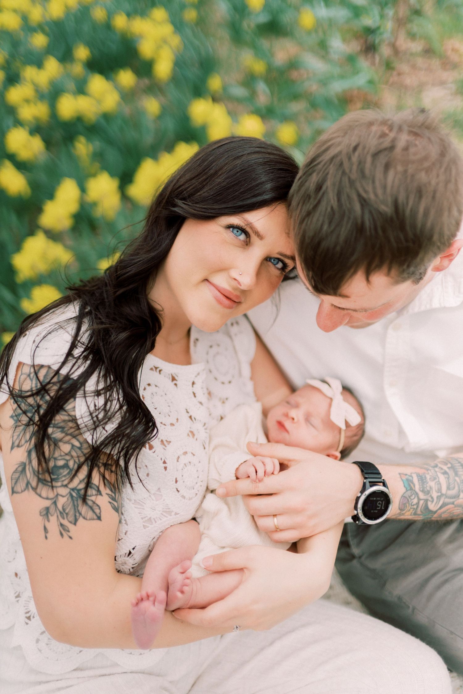A woman in a white lace dress holds a sleeping newborn baby in this tender black and white portrait.