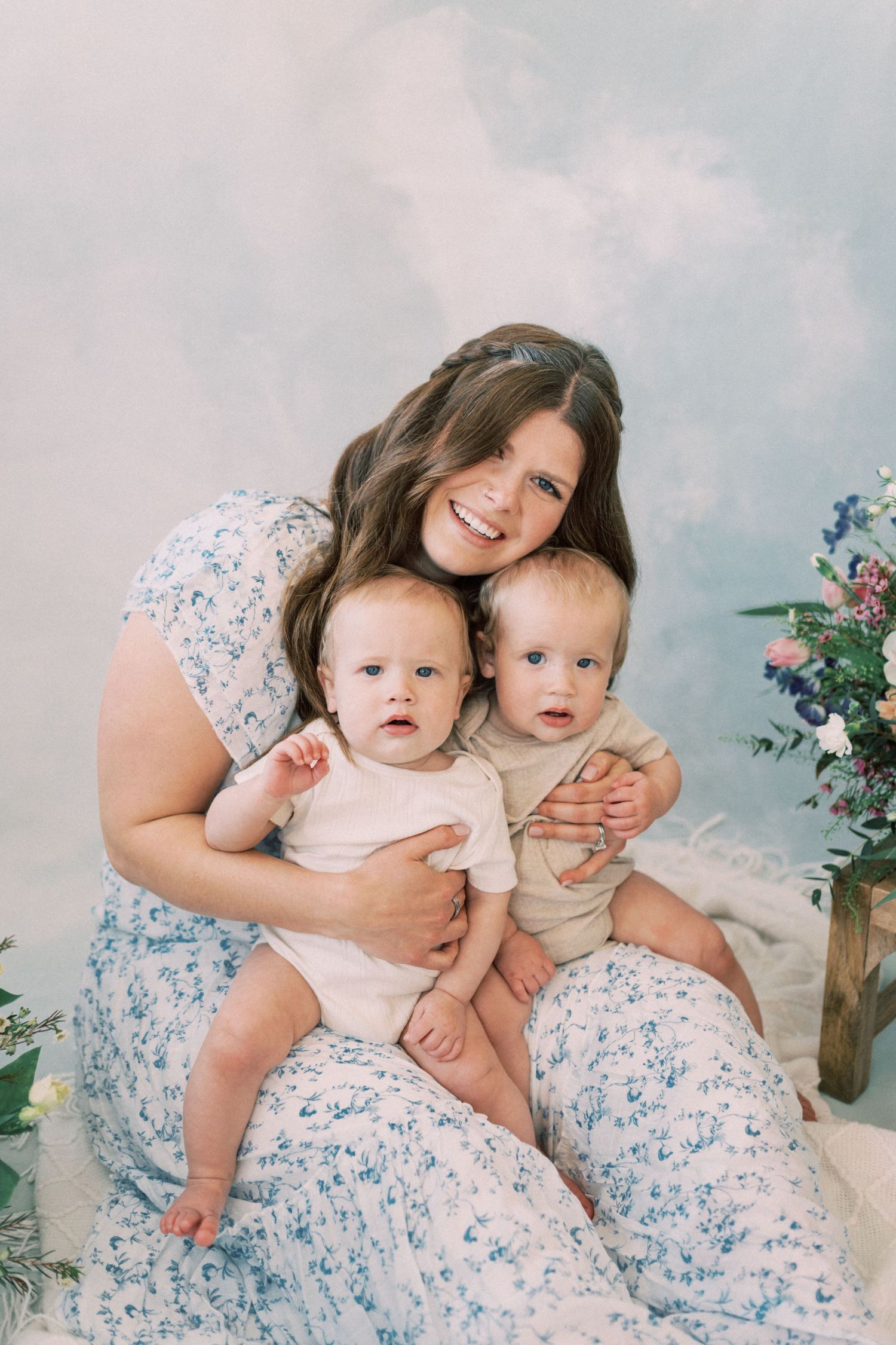 Sweet spring portrait of mother and baby surrounded by pink and blue flowers against a light dreamy background.