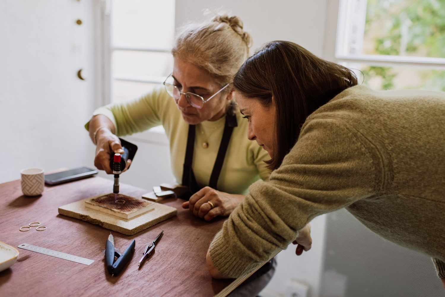 Two people lean over a workbench examining detailed craftwork together.