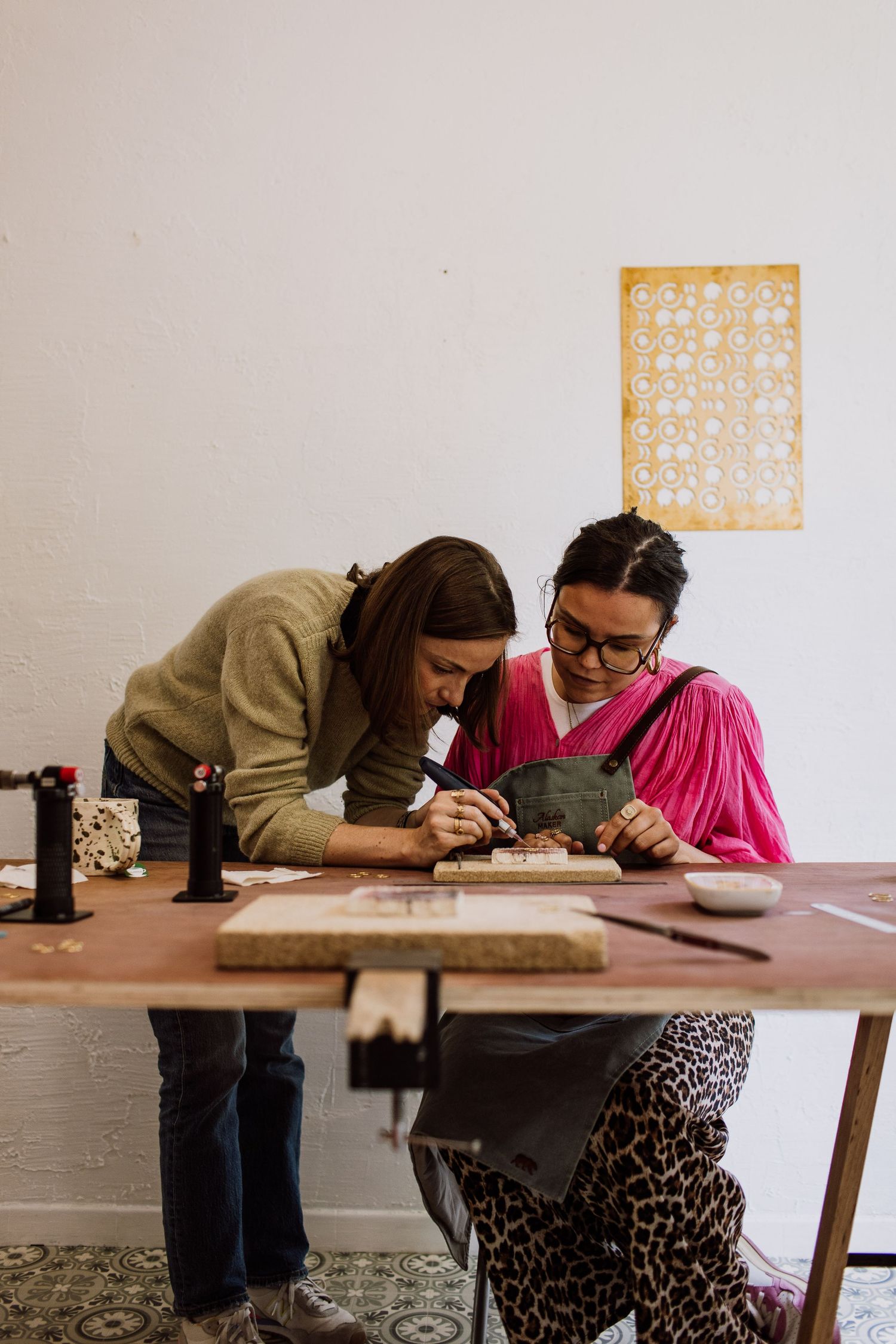 Students practicing jewelry making techniques at a workshop table with tools.
