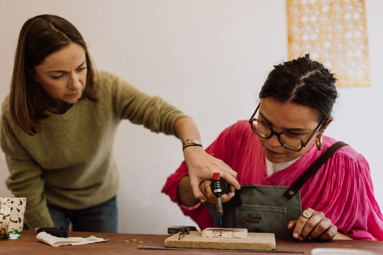 Two artisans collaborating on a detailed jewelry project at a wooden workbench.