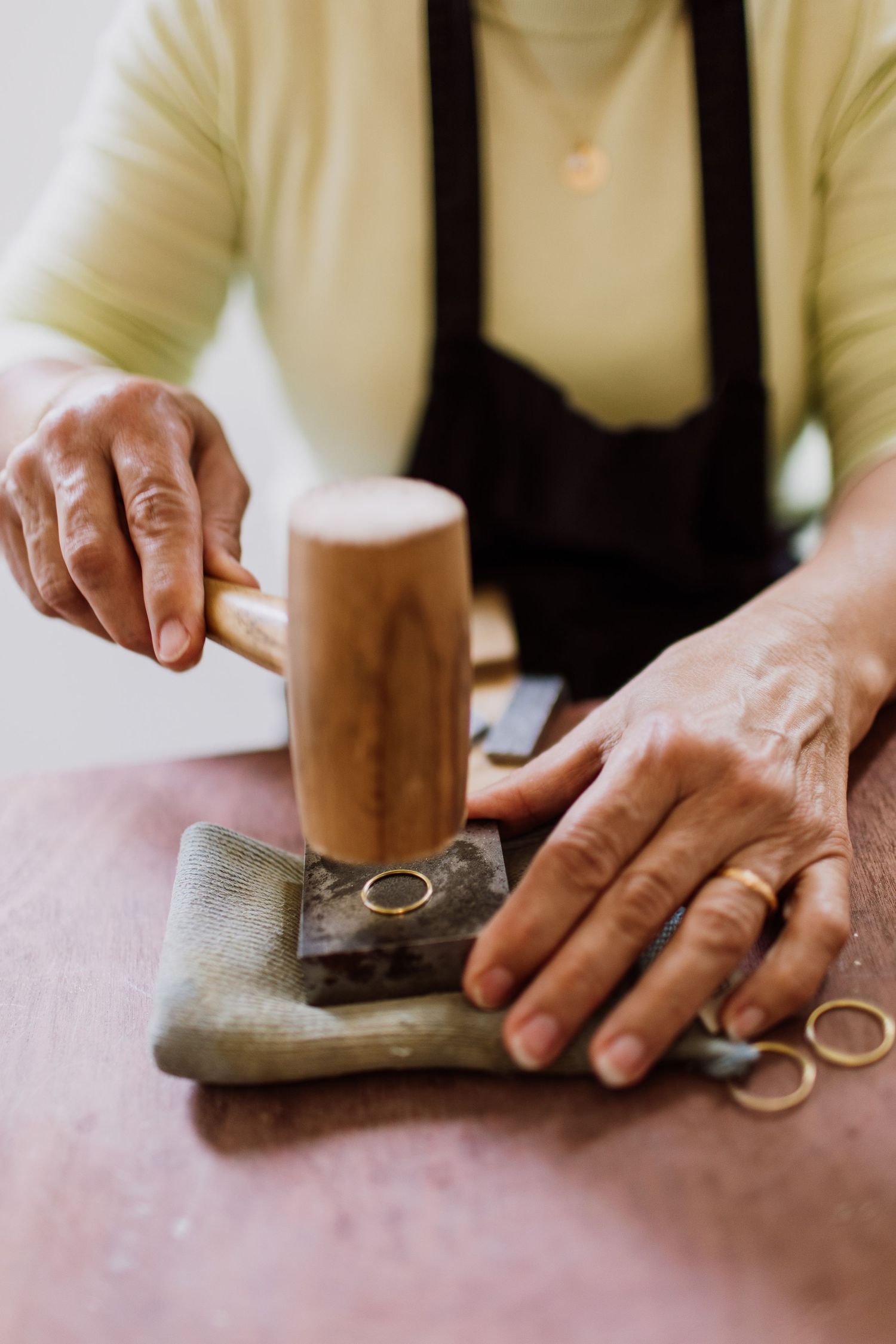 Hands working with a wooden mallet and jewelry tools on a leather pad.
