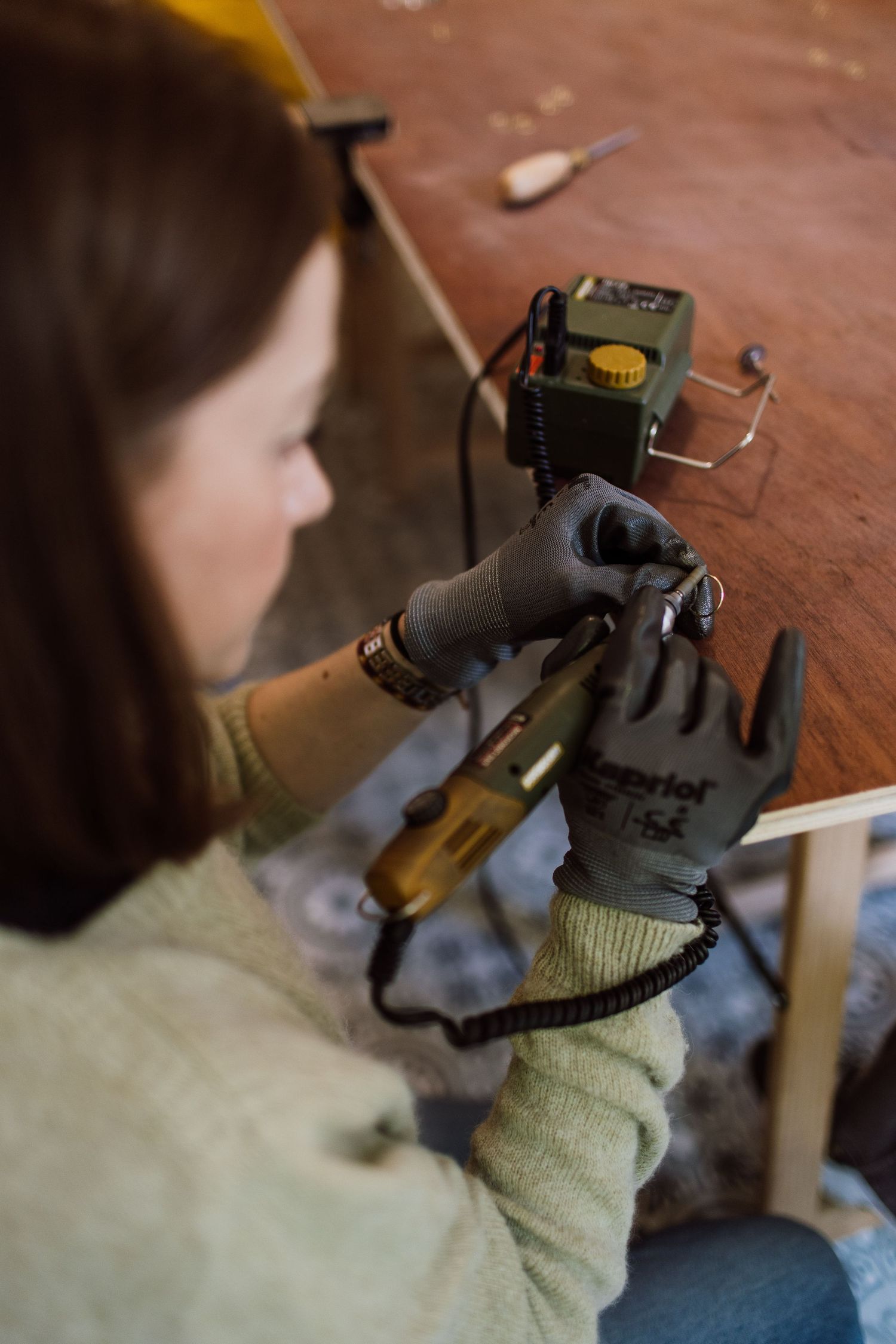 Close-up of hands wearing work gloves while using crafting tools on a wooden surface.