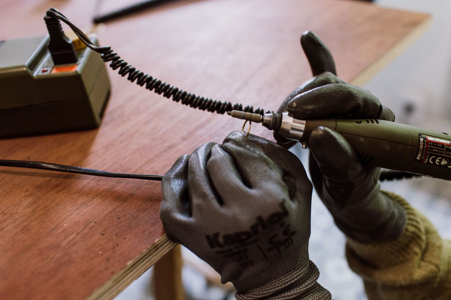 Close-up of gloved hands working with a coiled black cord on wooden surface.
