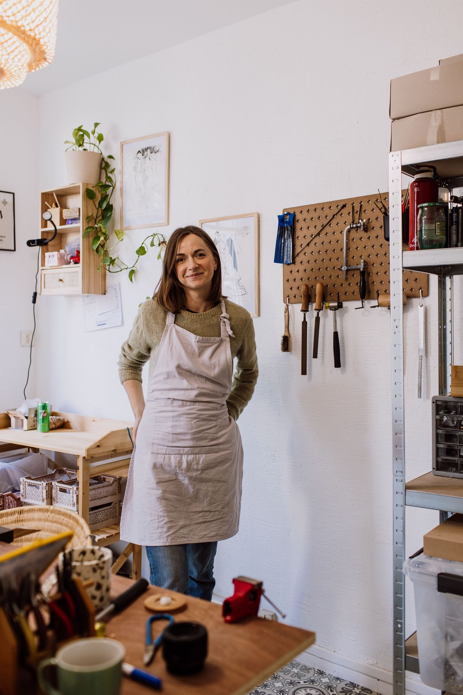 Craftsperson wearing beige sweater and apron standing in organized workshop studio.