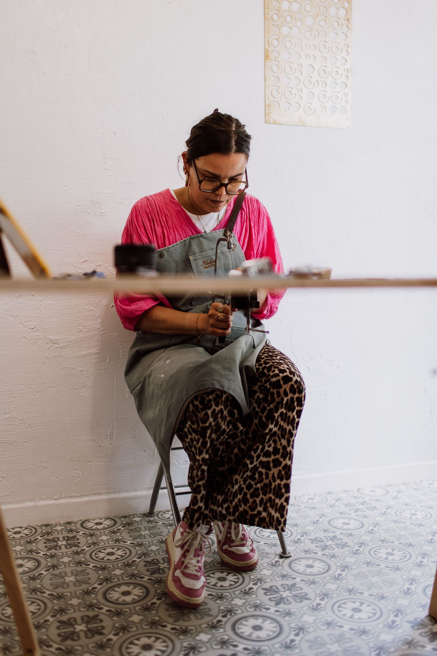 Creative workspace with person in pink top and overalls working on craft project.