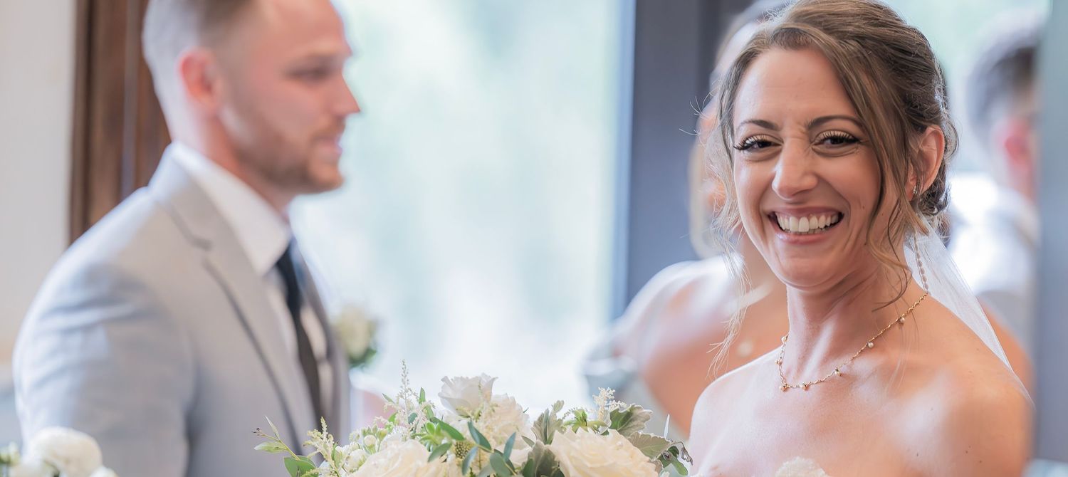 Gorgeous bride smiling with joy and laughter on her wedding day, her husband elated in the background, St. James, Utica, 2024