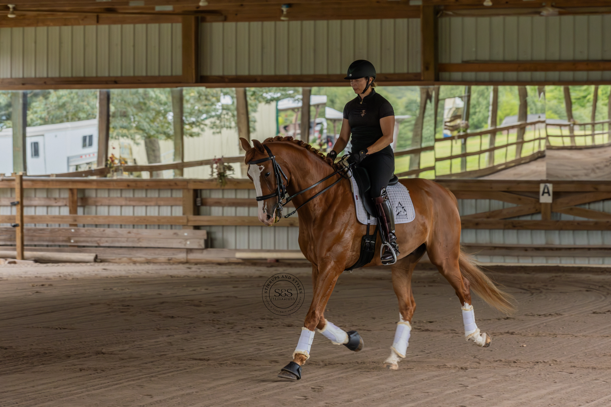 Rider trains dressage horse in covered arena with professional equipment.