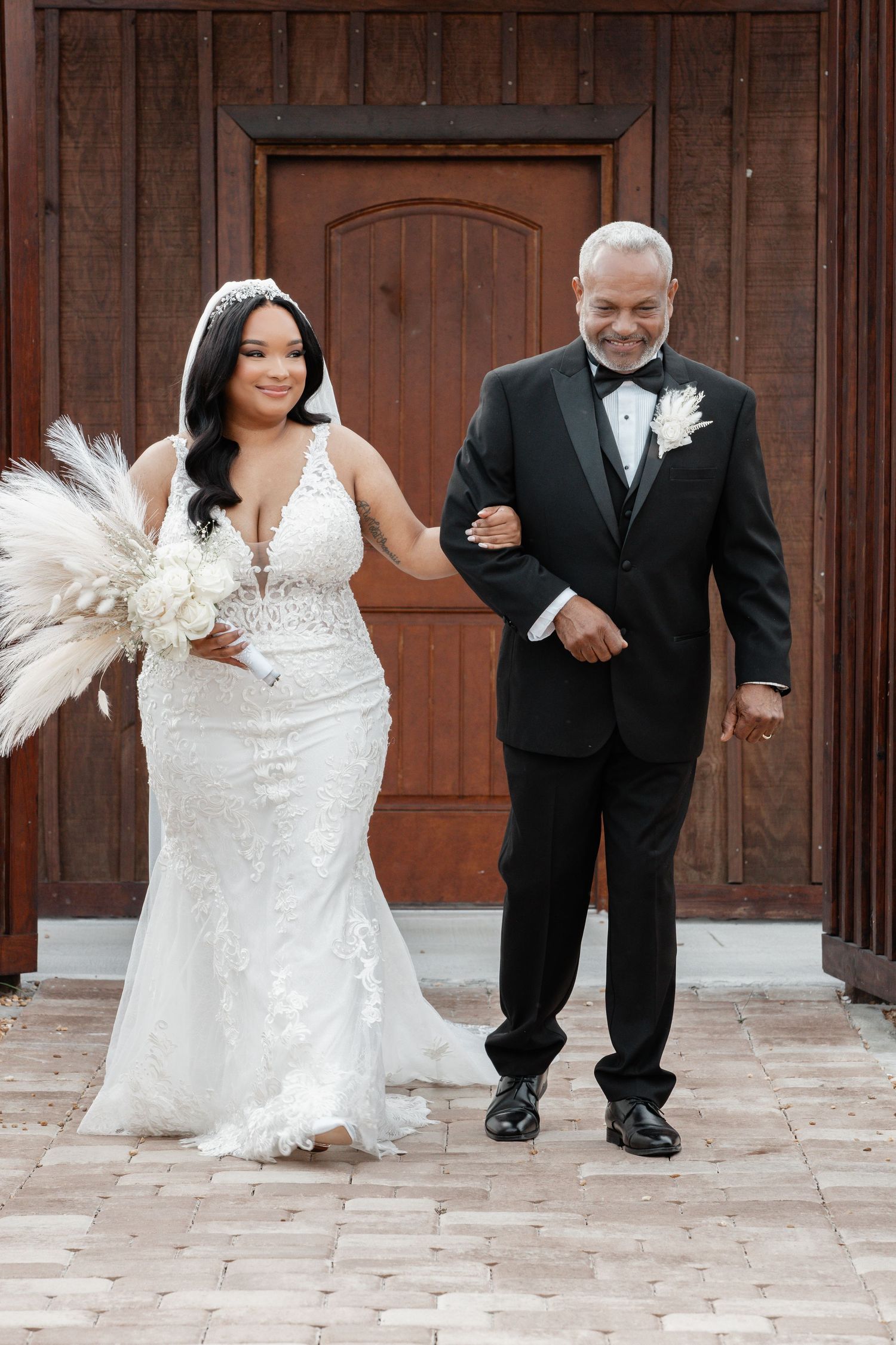 Traditional wedding portrait in front of wooden doors with elegant attire and pampas grass decor.