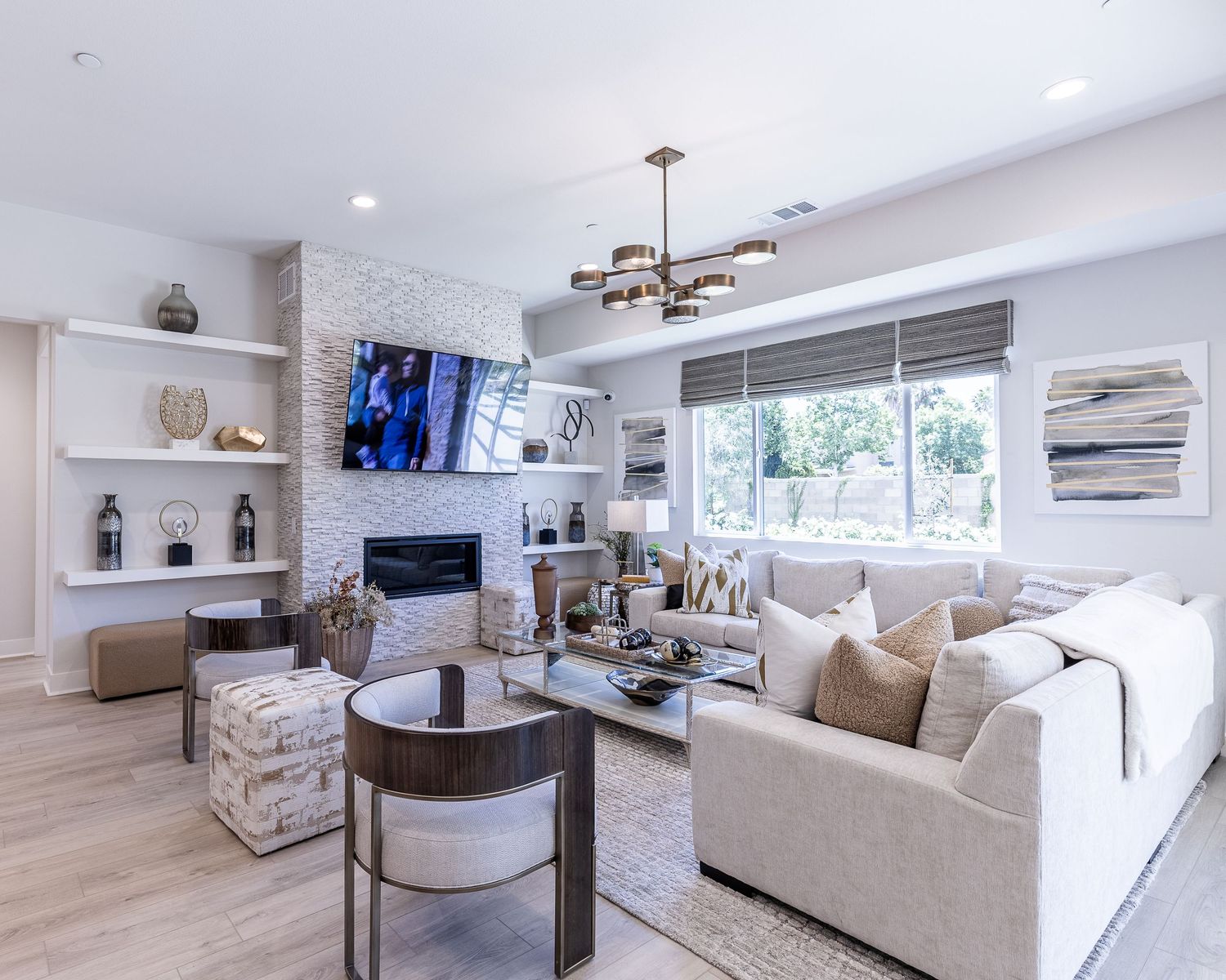 Modern living room with light hardwood floors, sectional sofa, mounted TV, and contemporary light fixture above.