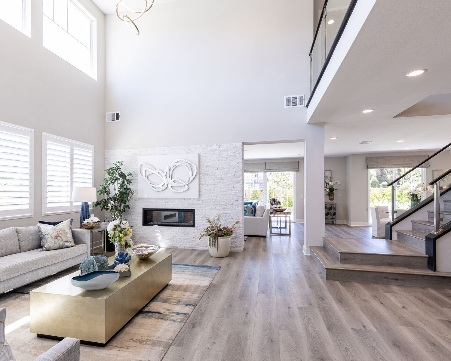 Modern open concept living room with high ceilings, gray wood floors, and a minimalist fireplace beneath a geometric wall art.