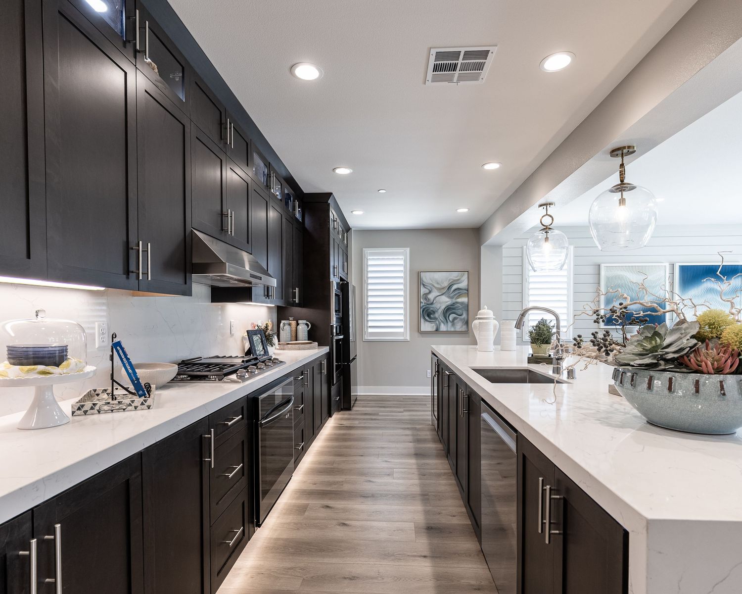 Real Estate Photo. Modern kitchen, dark cabinets, white countertops, and hardwood floors features recessed lighting and pendant fixtures.