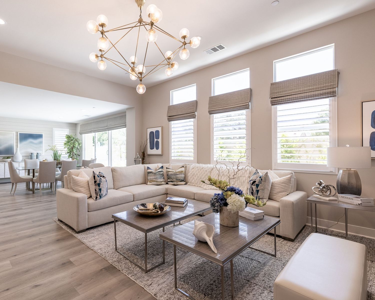 A modern living room with high windows, beige sectional sofa, wood floors and geometric chandelier in natural lighting. Located in Palmdale.