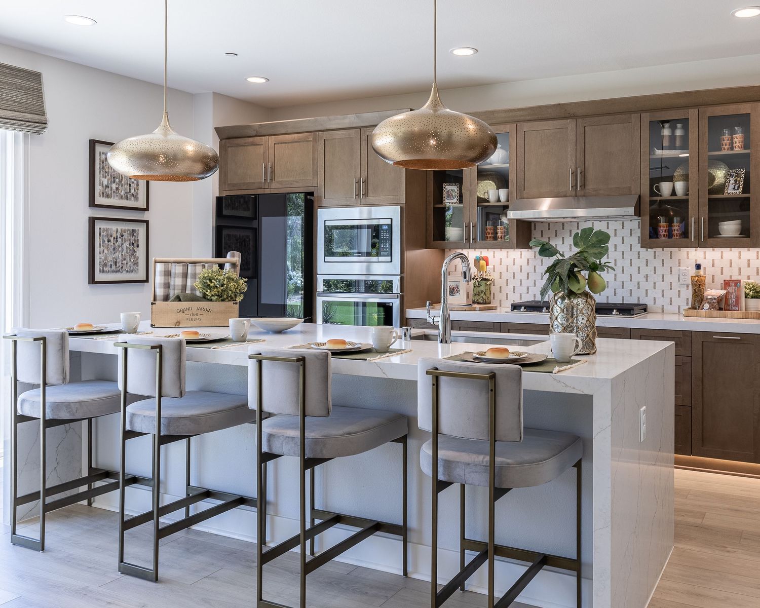 Modern kitchen with gray cabinets, white quartz island, metallic pendant lights and contemporary black bar stools.