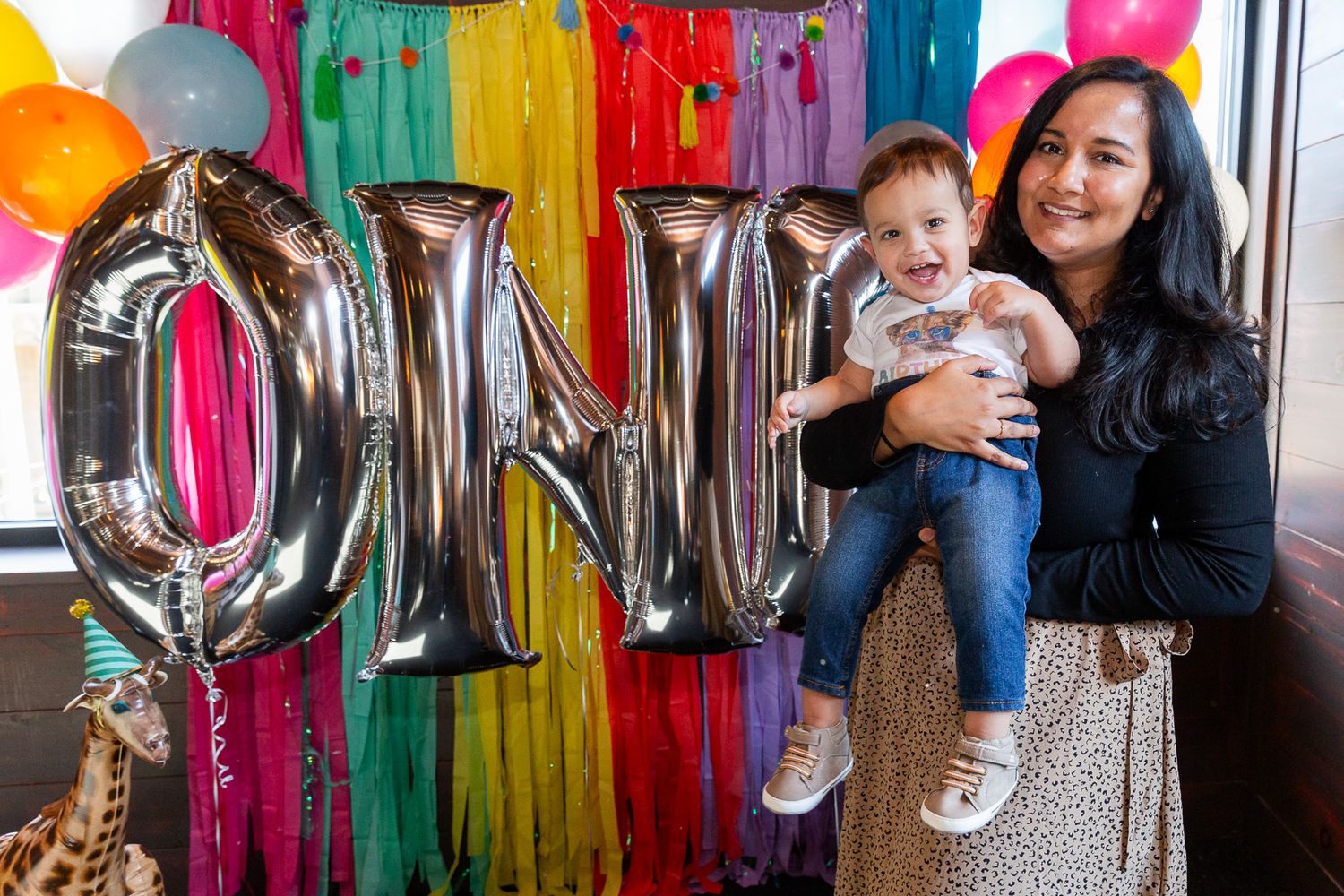 Party celebration with silver ONE balloon letters against colorful streamer backdrop.