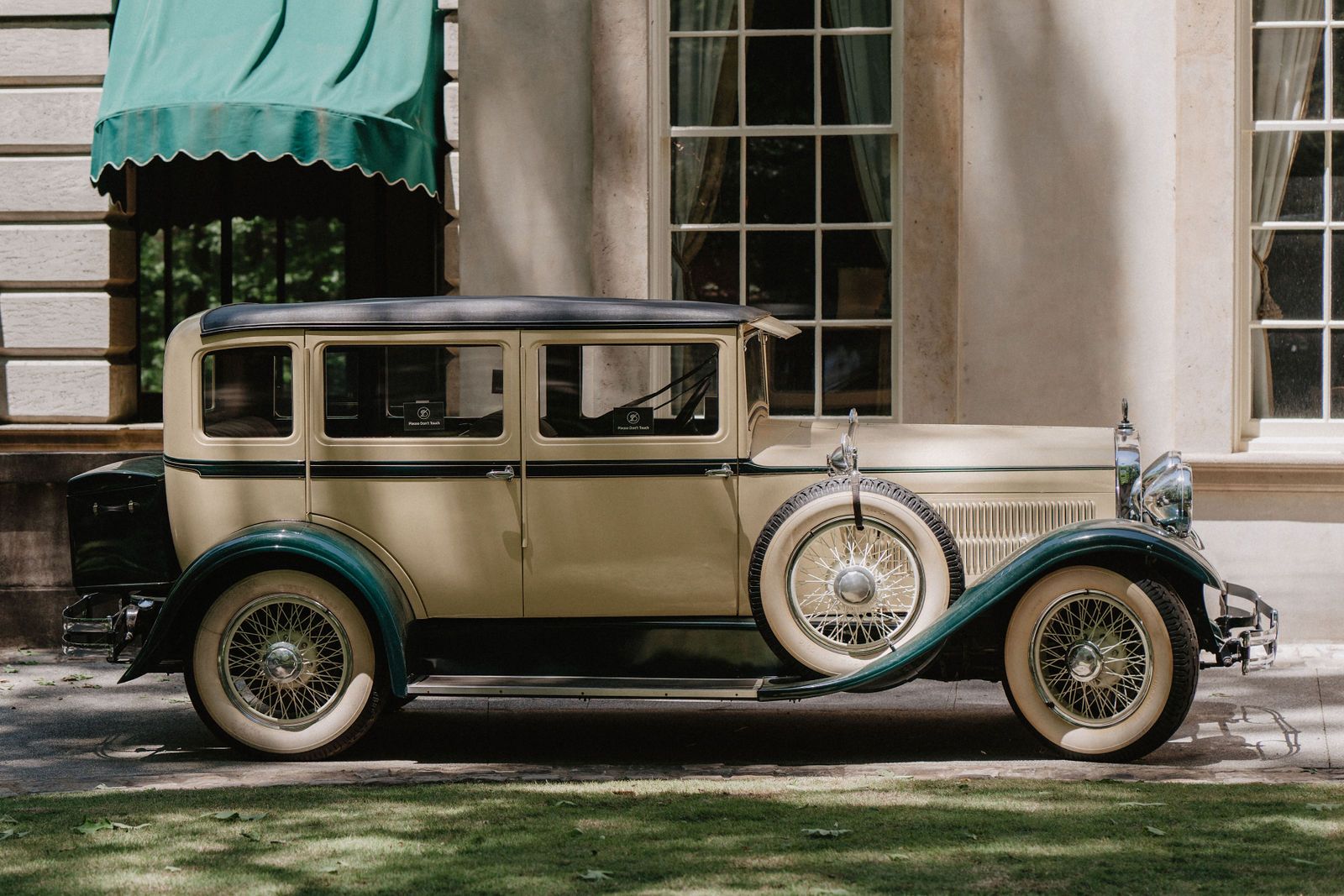 Vintage cream-colored 1920s luxury car parked outside a classic building.