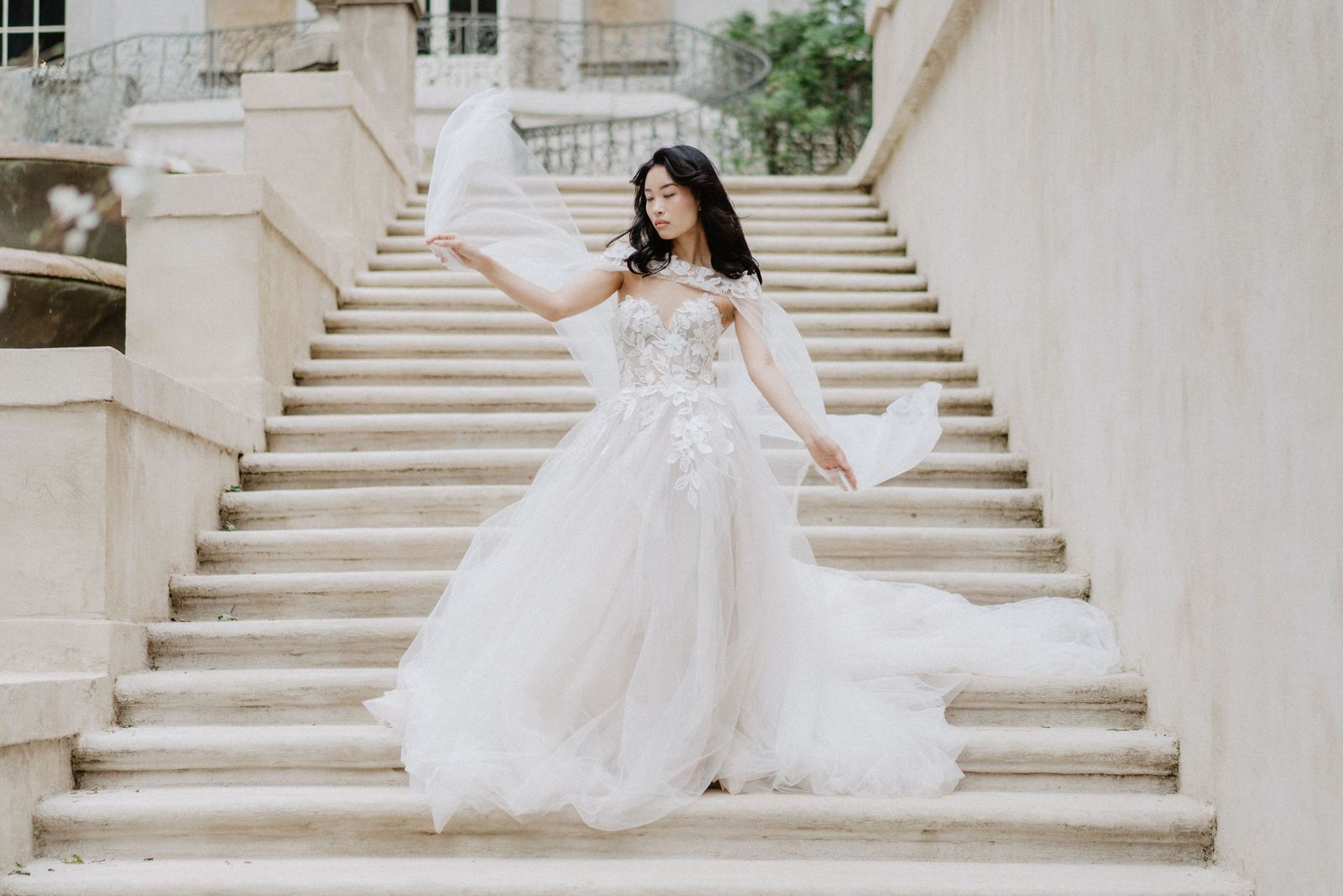 A flowing white wedding gown showcased on grand stone steps of a mansion.