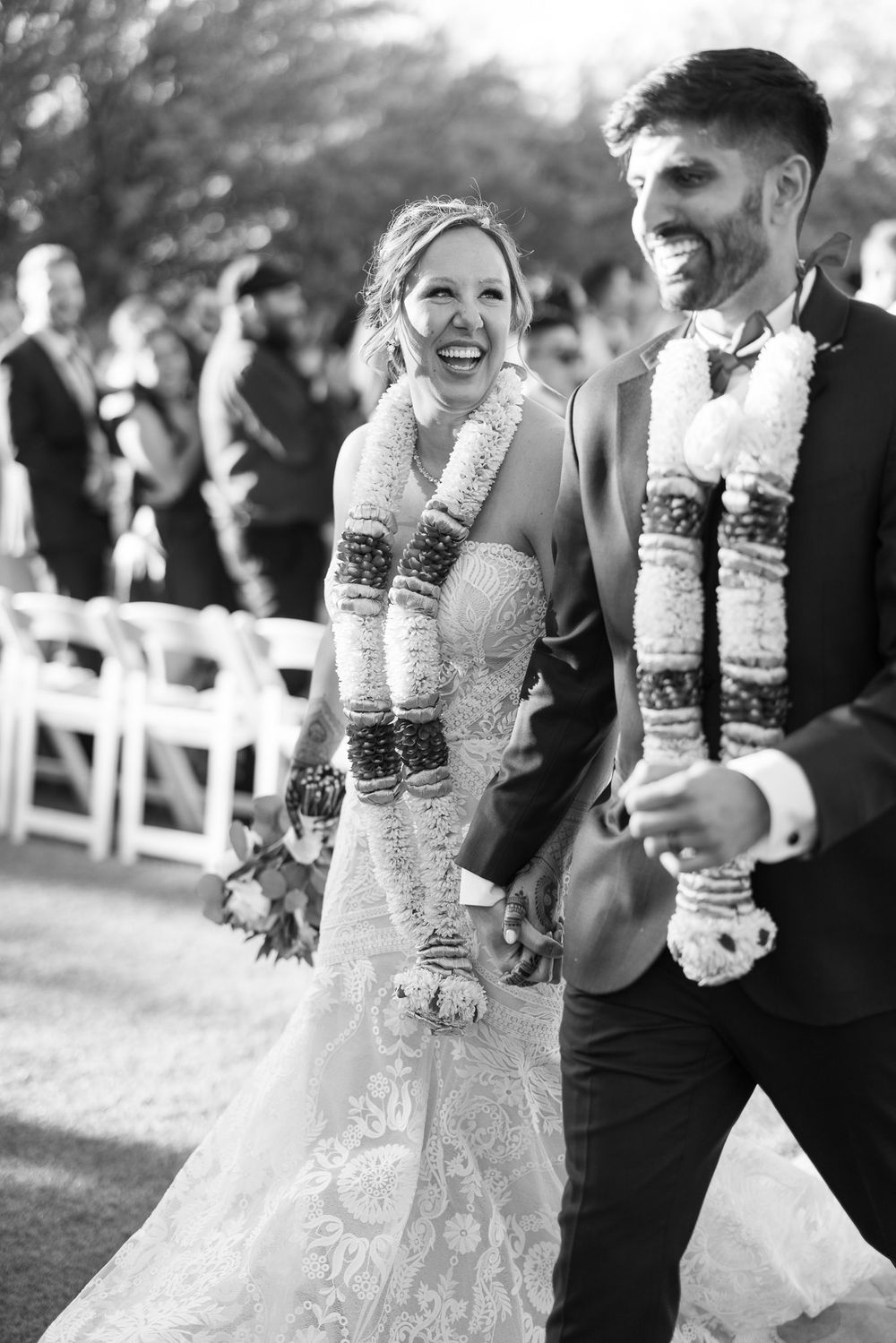 Newlyweds share a joyful moment wearing traditional floral leis and wedding attire at an outdoor ceremony.