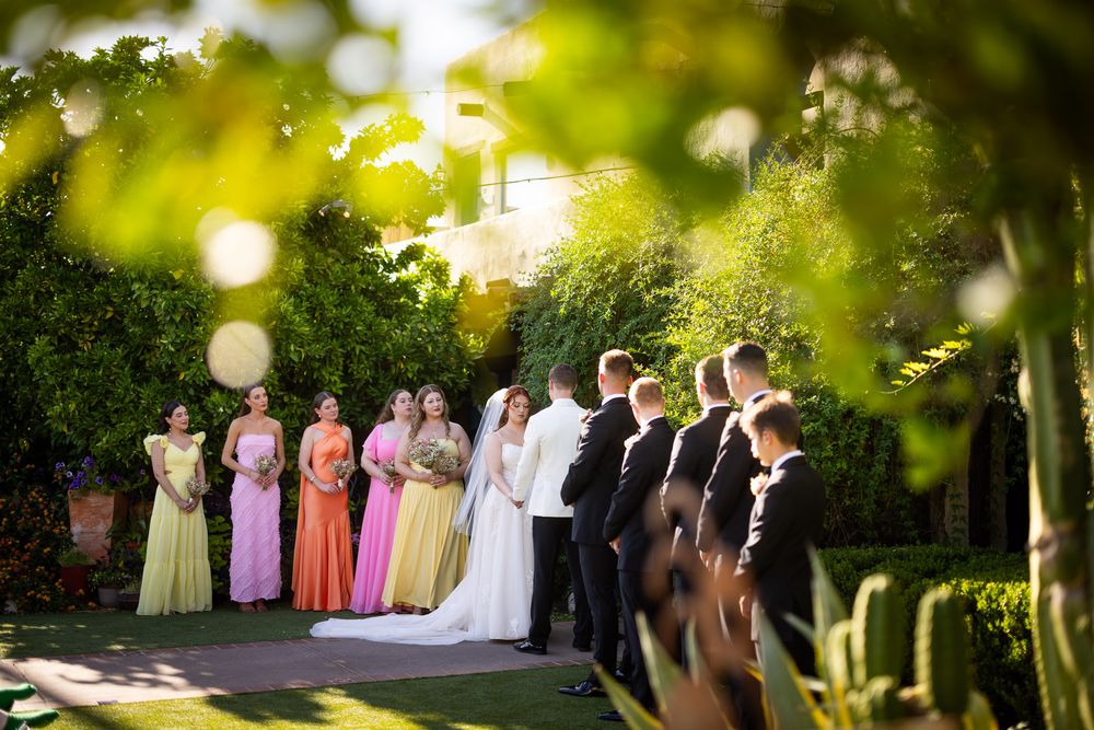 Wedding party line stands outdoors in a sunny garden setting with bokeh lighting effects.