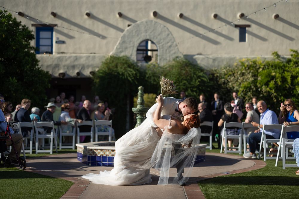 Elegant outdoor wedding ceremony scene with couple performing romantic dip kiss in front of seated guests.
