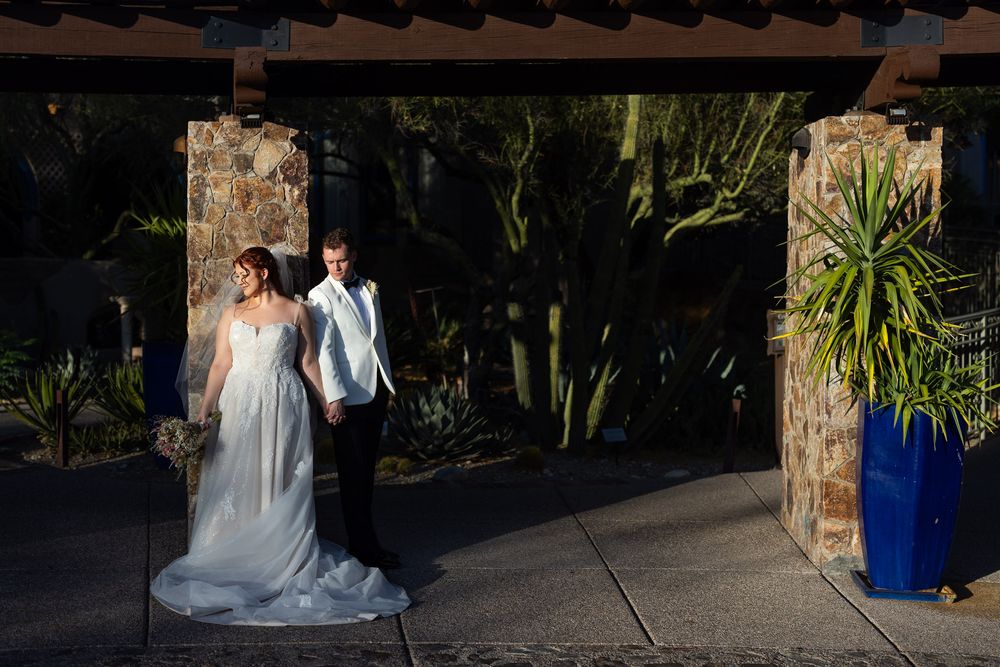 Newlyweds walk under a covered stone walkway with desert landscaping.