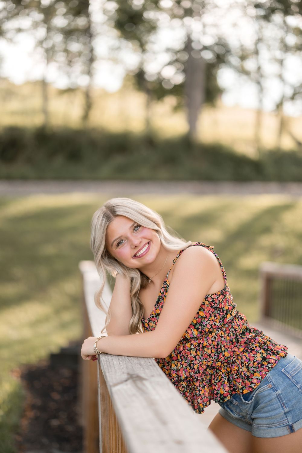 A floral top paired with denim shorts creates a casual summer look in an outdoor setting with soft natural lighting.