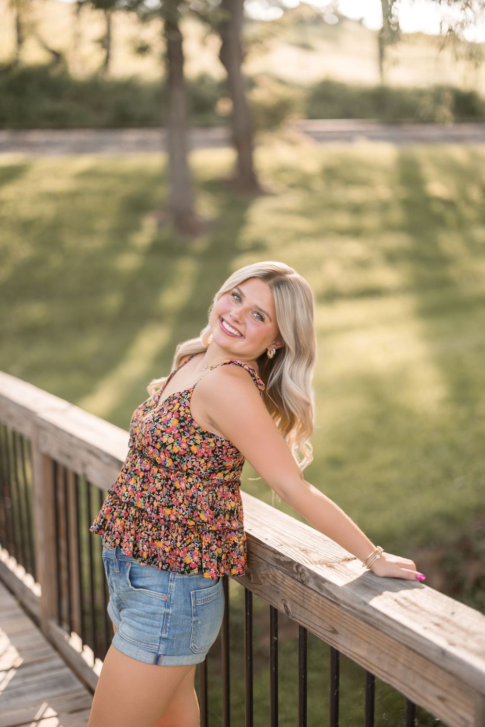 Summer outdoor portrait on a wooden bridge deck wearing a floral top and denim shorts.