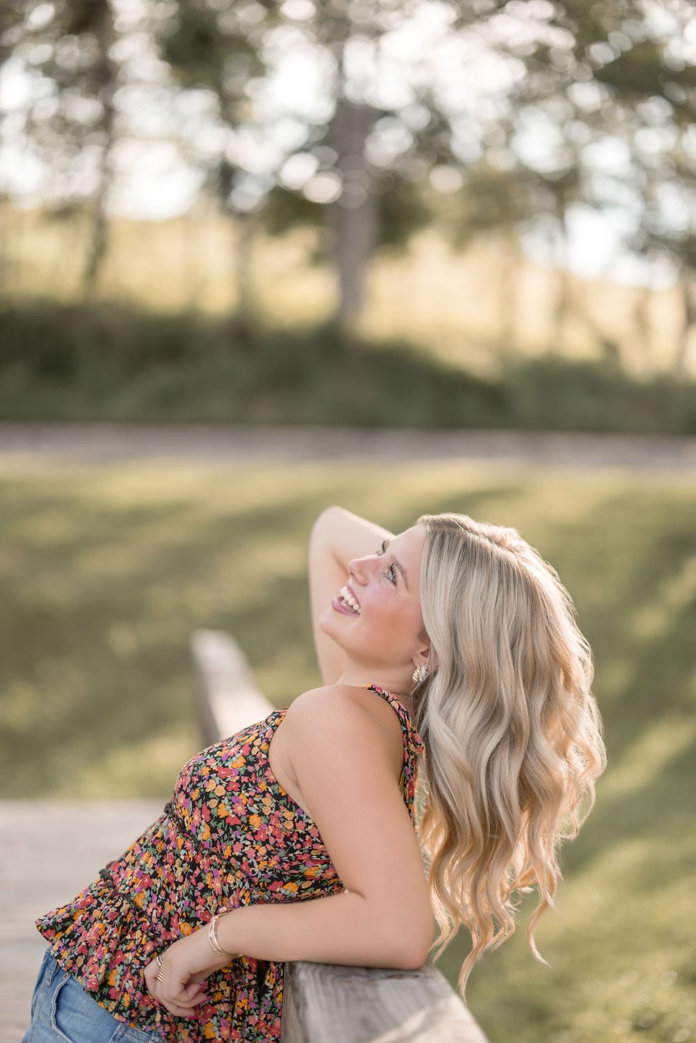 Joyful person in floral tank top and denim leaning back in laughter against golden sunset background.
