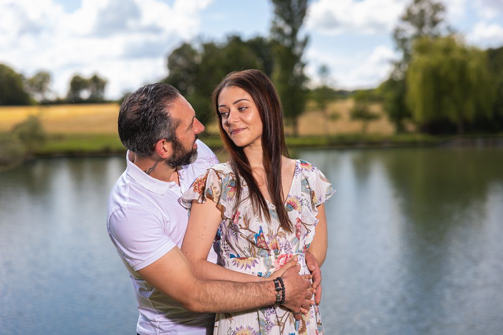 A couple shares an intimate moment together by a serene lake during golden hour.
