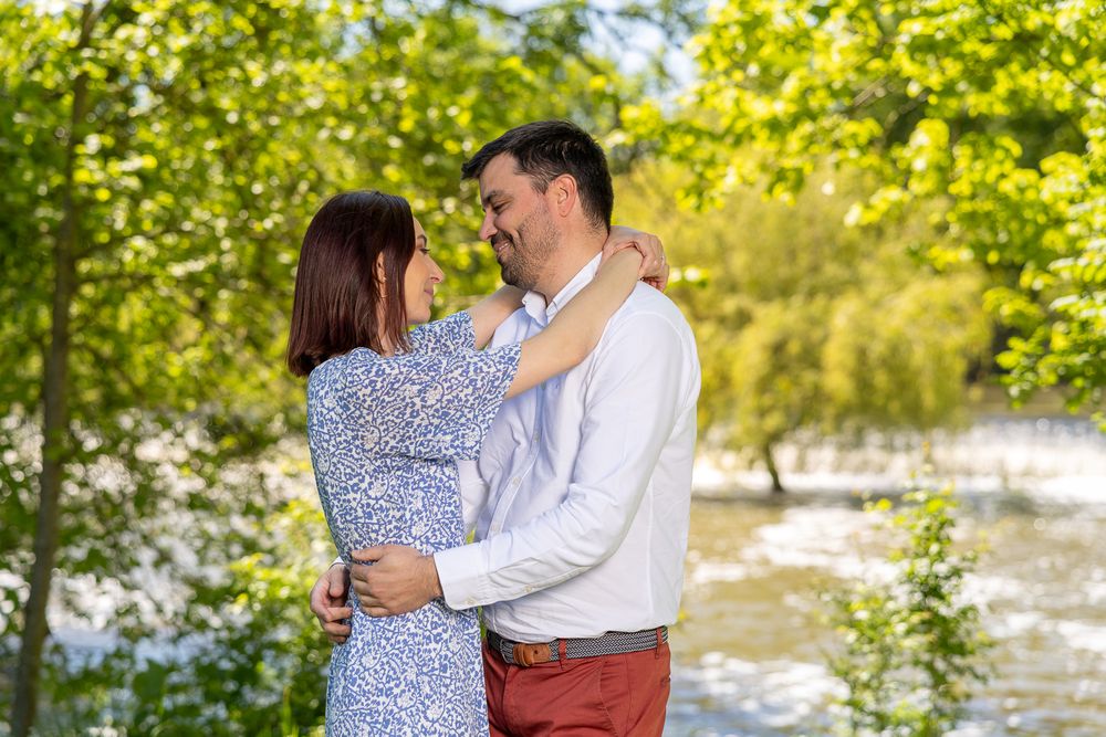A couple dancing outdoors in a romantic setting with sunlit trees and greenery in the background.