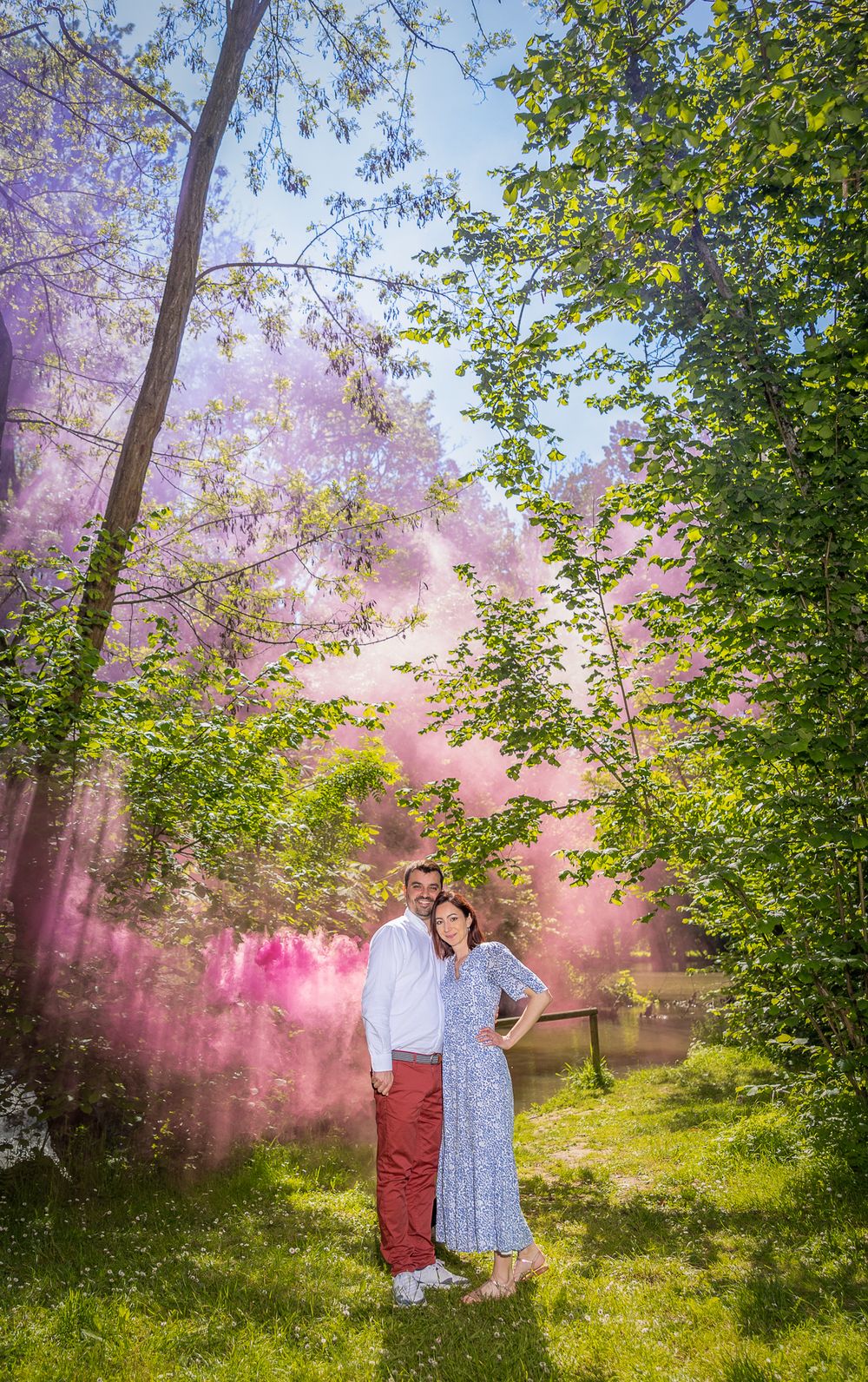 A romantic couple embraces in a dreamy forest setting filled with pink smoke and vibrant green foliage.